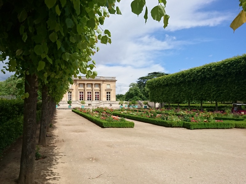 Schlosspark Versailles mit dem kleinen Schlösschen Petit Trianon im Hintergrund, Beete mit Blumen, Hecken und Bäume.