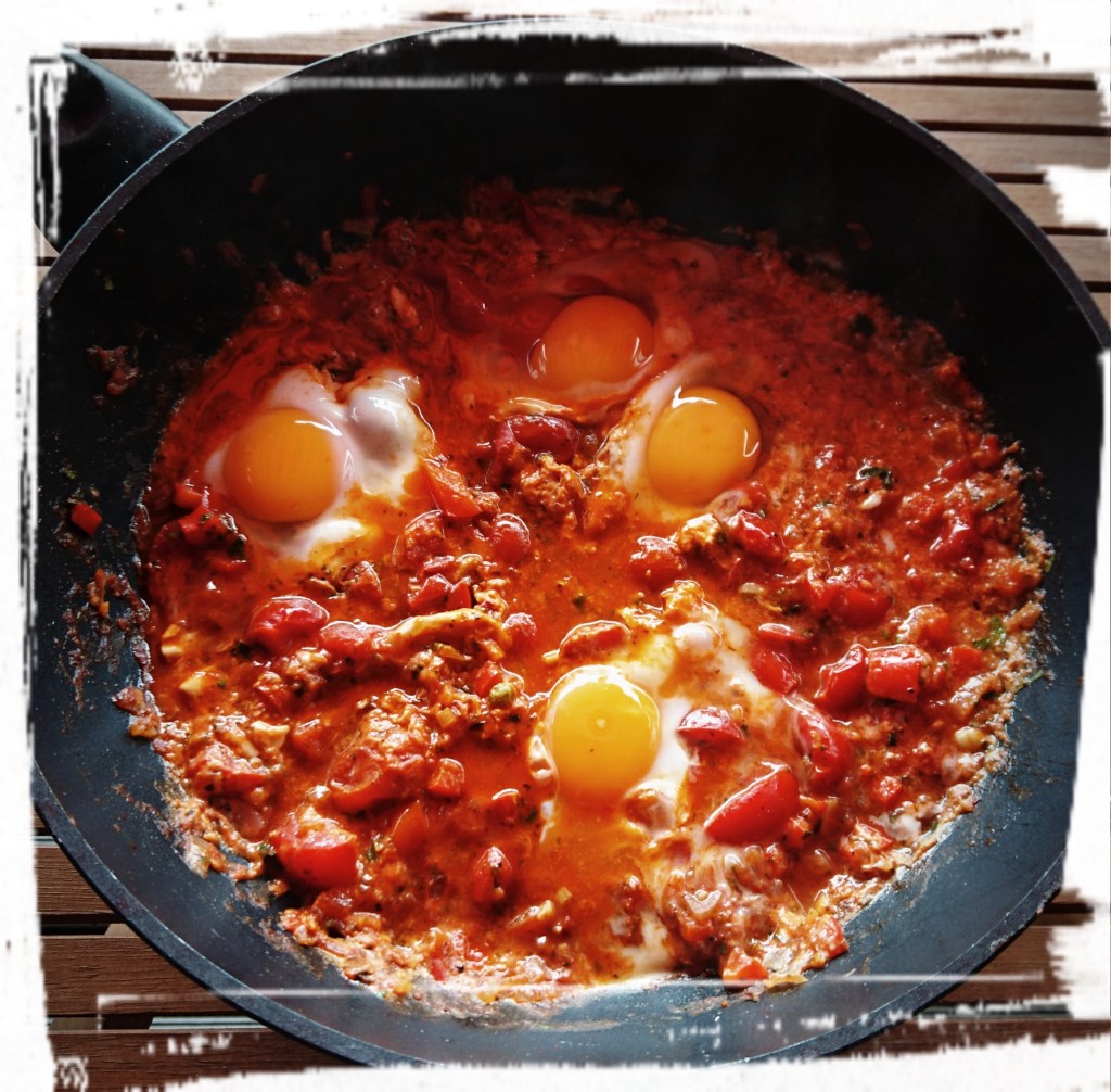 Eine große Pfanne mit dem Tomatensud, darin vier noch rohe Eier.