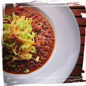 Gekochte Bolognese mit Bandnudeln in einem runden Teller. Die Farbe ist wunderbar rötlich.