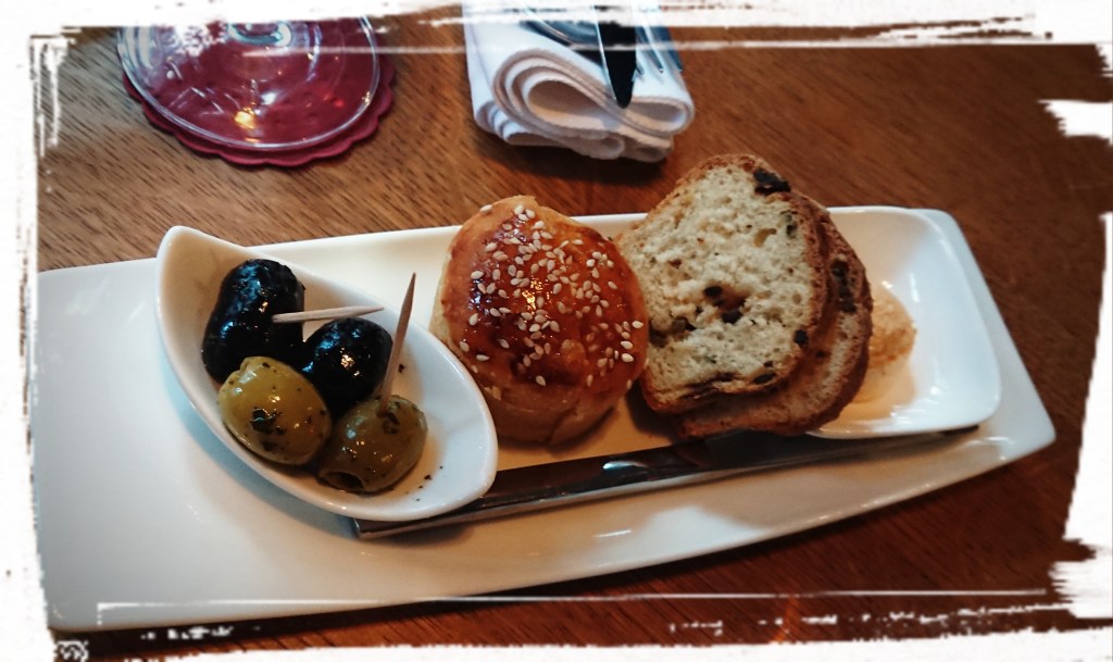 Frisch gebackenes Brot und Oliven auf einem schmalen Teller angerichtet.
