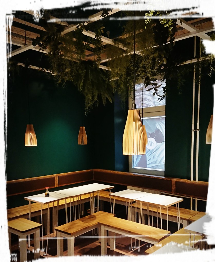 Dunkelgrüne Wände, Holzlampen und Tische in Hell. Gemütlich und modern.