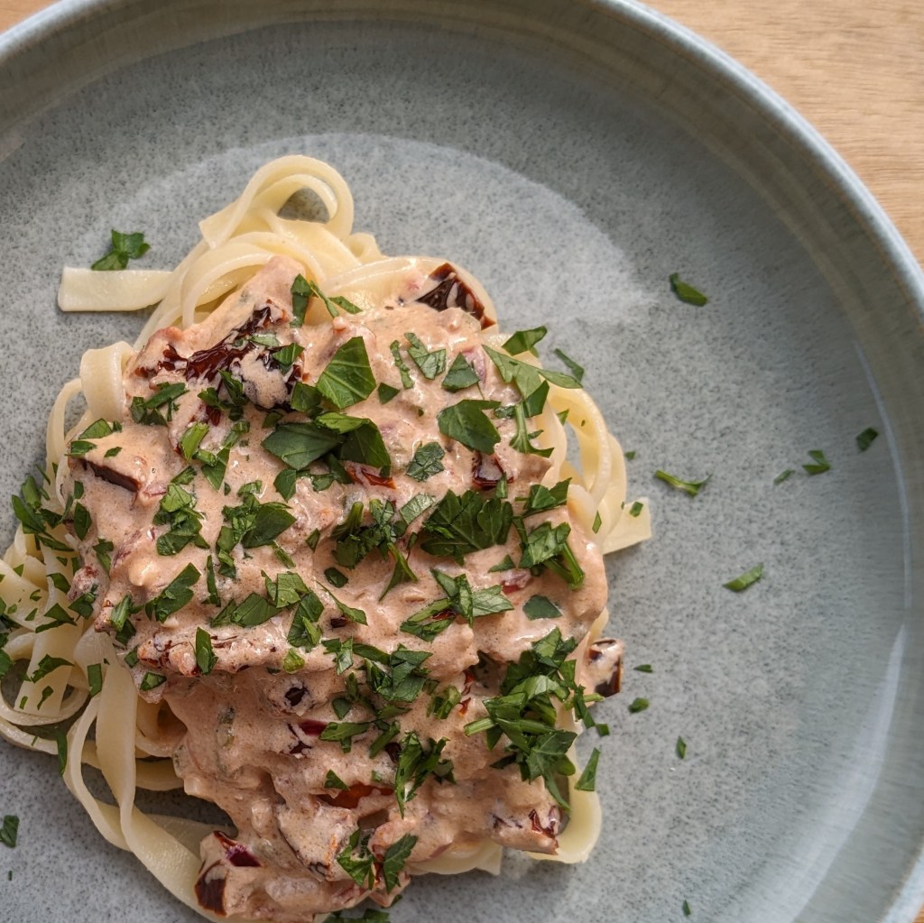 Auf einem runden Teller angerichtete Pasta mit Feta-Sauce mit getrockneten Tomaten und Petersilie.