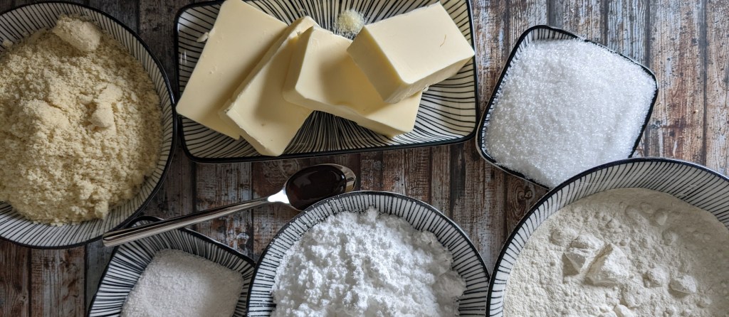 Mandeln, Butter, Zucker, Vanille, Puderzucker und Mehl in kleinen Schalen