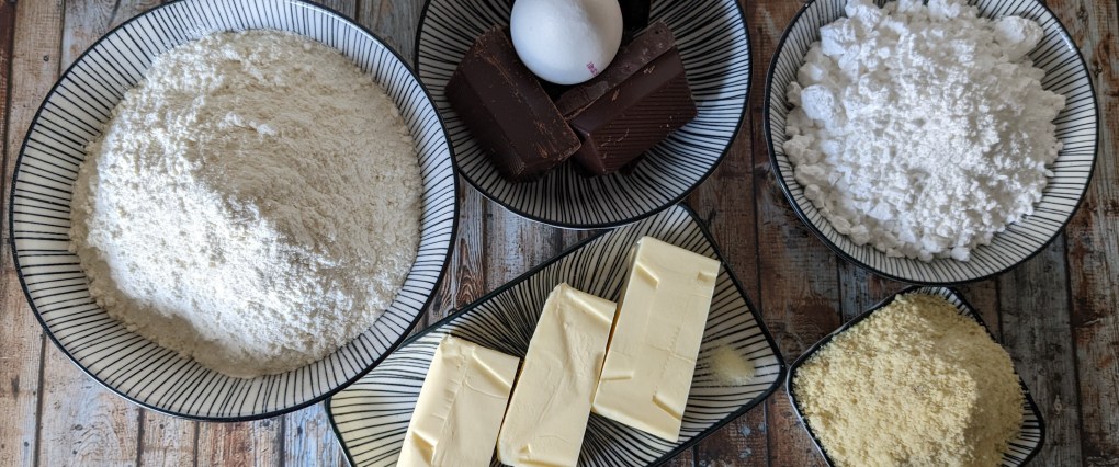 Schokoplätzchen-Zutaten: Mehl, Butter, Schokolade, Ei, Puderzucker, Mandeln