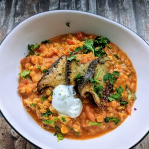 Weiße Schale mit rotem Linsencurry. Darauf gebratene Pilze und ein Klecks Crème fraîche.